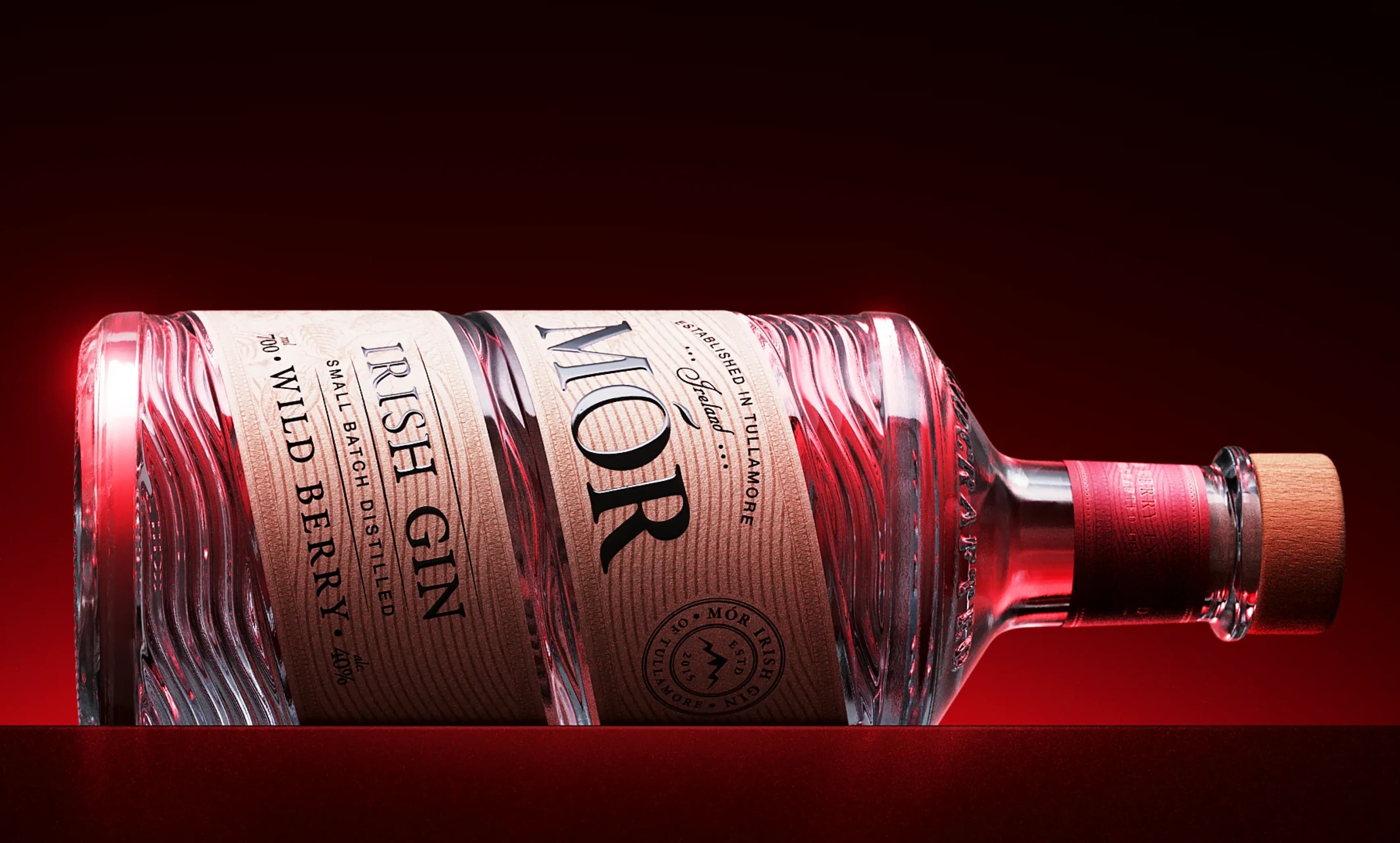 A ribbed glass bottle of MOR Irish Gin, Wild Berry, lying on its side in deep red light, a rim highlight running the length of the fluted glass.